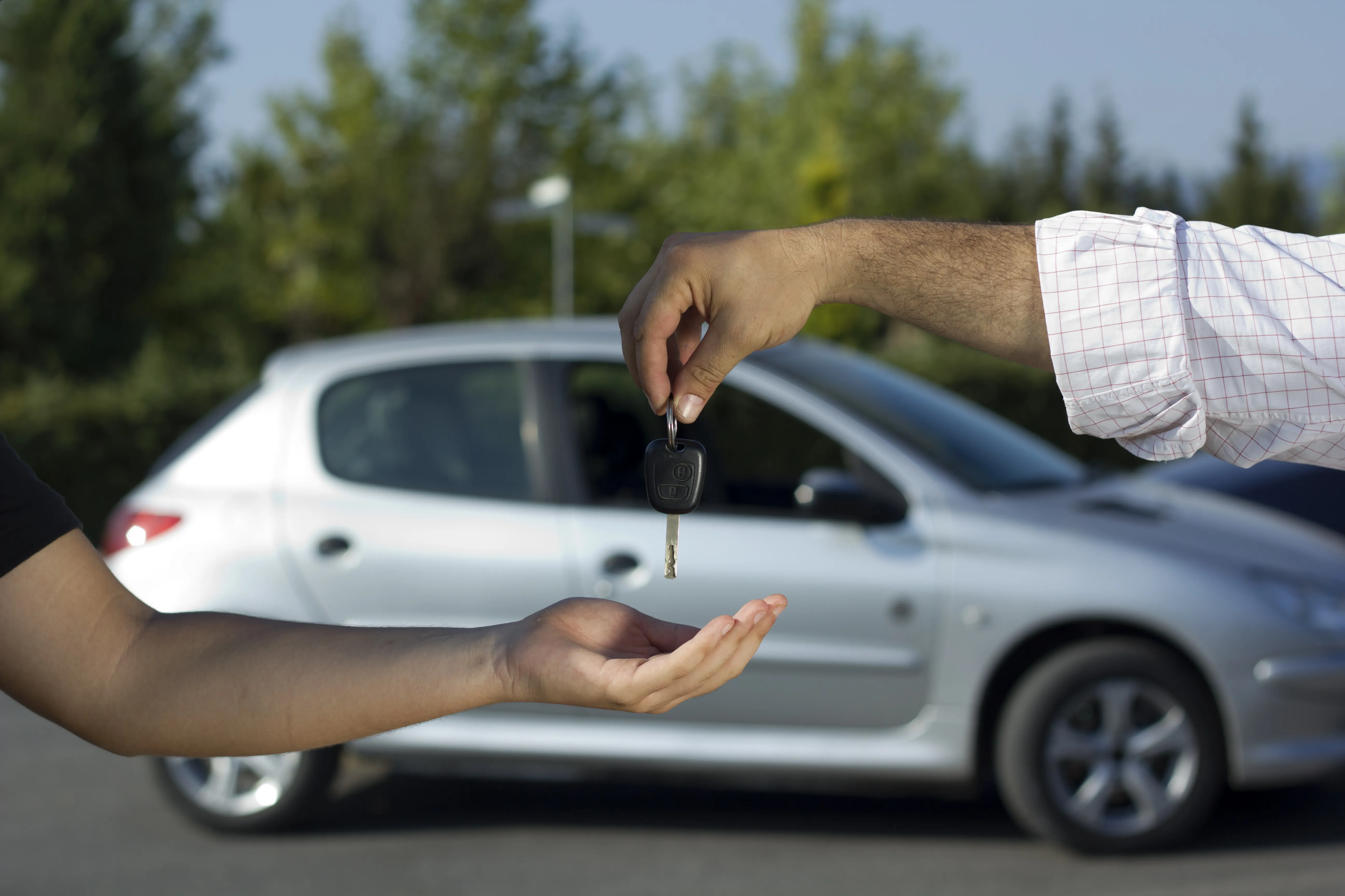A set of car keys held out over an open hand, a car behind