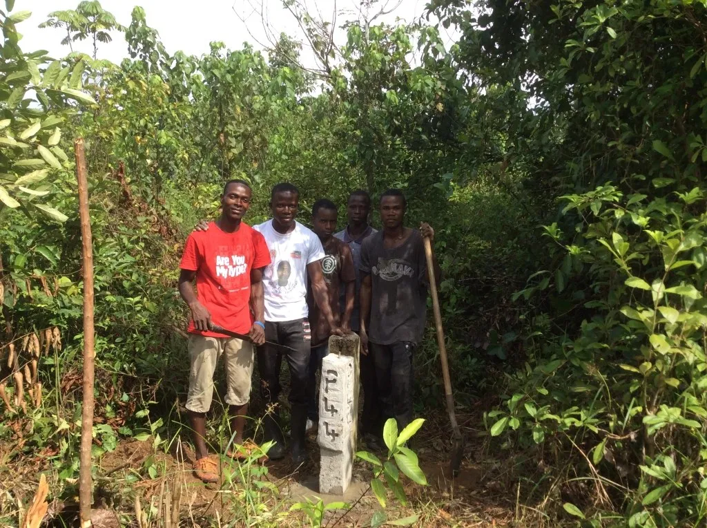 Young men standing beside a surveyed corner marker on the Kakata land